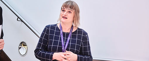 Photograph of a woman wearing a purple lanyard taken on a staircase against a white wall.