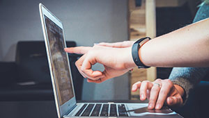 Two people using a laptop. Only their hands are visible. One hand points at the screen.