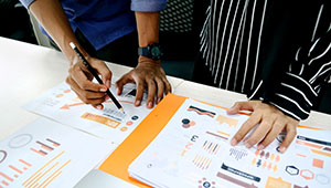 Two people working with some documents displaying charts and figures. Only their hands are visible.