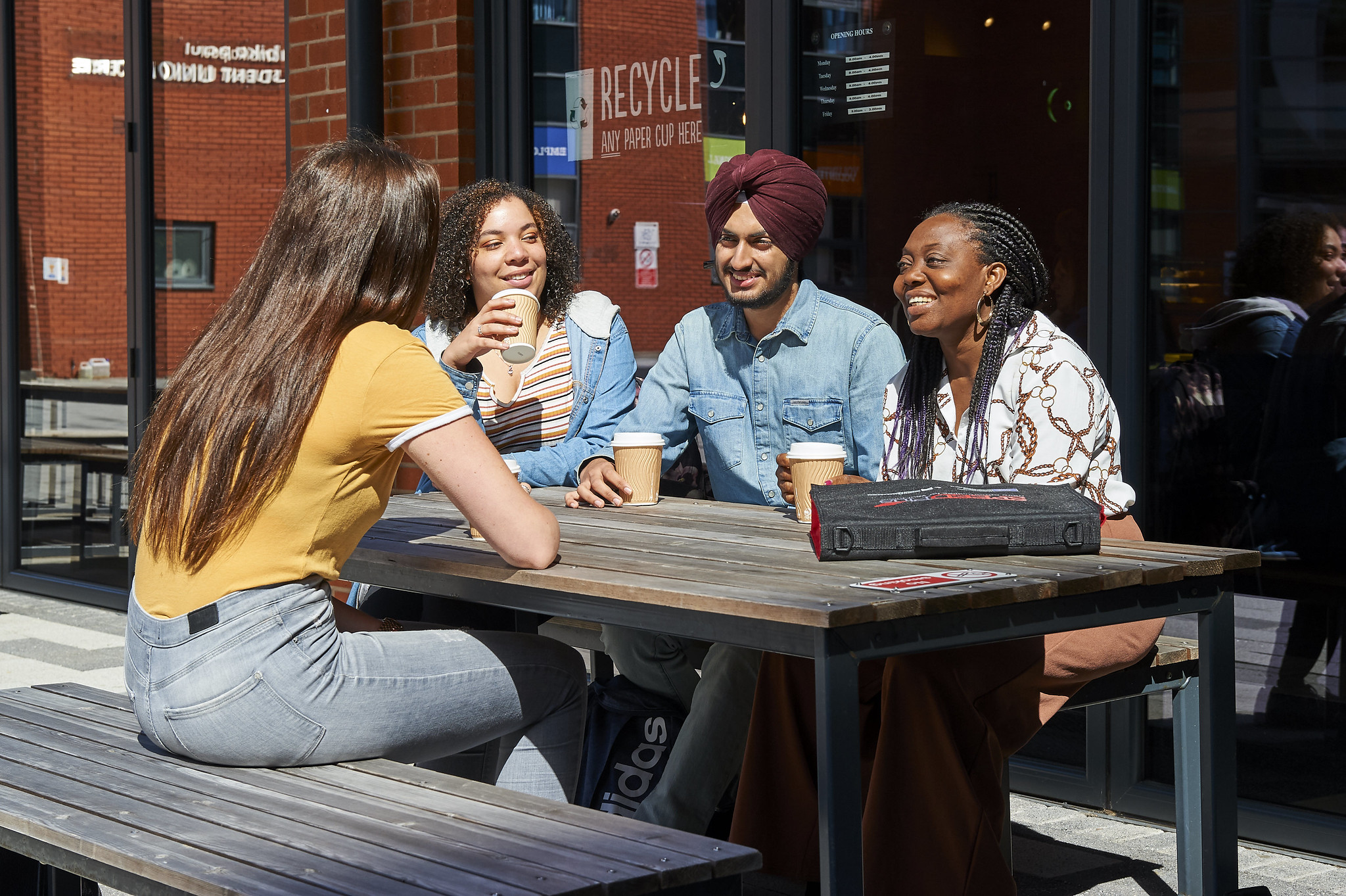 Students sitting around a bench in the City Campus courtyard and drinking coffee