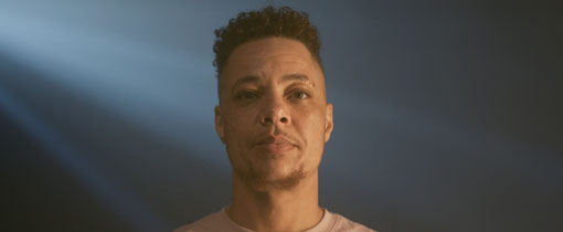 Nate Ethan Watson wearing a white shirt against a backdrop of projected images