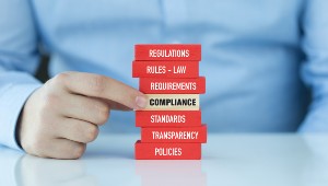 Man 's hand pointing to a red wooden block within a stack that says compliance