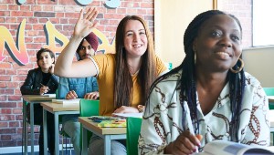 Four students in a classroom, one student has their hand up