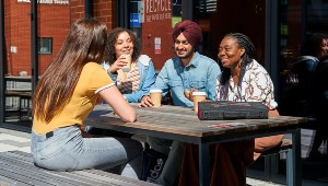 Students drinking coffee together at an outdoor table in the courtyard of Wolverhampton City Campus