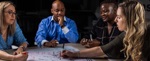 Students sitting at a work table, writing on a whiteboard together,