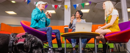 Two students sat down in a communal area, having a conversation using sign language.