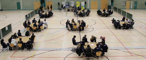Groups of people seated at various tables inside the Sports Hall.