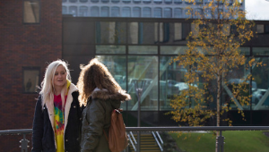 Two students outside a building in conversation with each other.