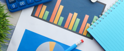 Image of printed graphs, post-it notes, a calculator and a pencil arranged on a tabletop.