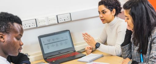 Students sitting together at table with laptop talking