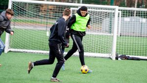 Three males on football pitch kicking ball