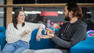 two adults sit on a couch and sign to each other