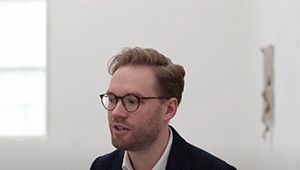 A person standing in a white gallery room, photographed in the IKON gallery