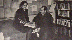 Black and white photograph of Beatrice Warde and another person, Warde reading from a large open book