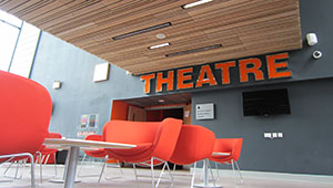 Red chairs and tables arranged in a lobby outside a room identified as a THEATRE via signage