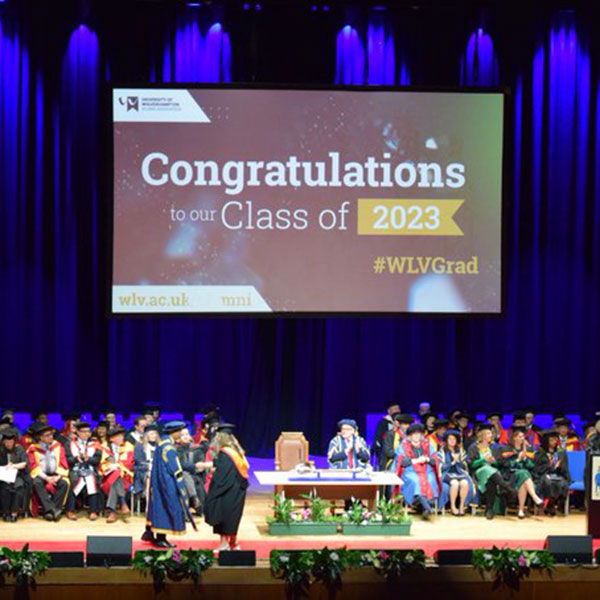 Photo of a graduation ceremony with a screen reading CONGRATULATIONS