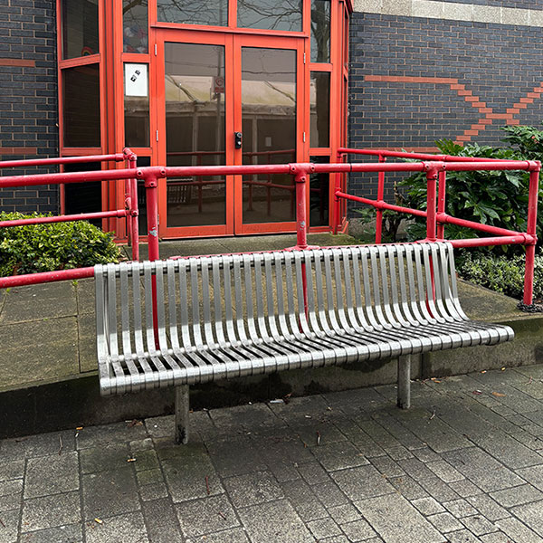 Photograph of a metal bench in front of a glass doorway with red frames.