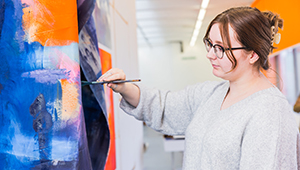 Female Fine Art painting in one of the Fine Art studios. They are wearing glasses on focusing intently.