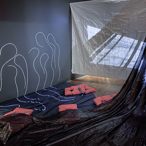 Photograph on an installation, with black plastic sheets, red life jackets and abstract figures projected onto a black screen