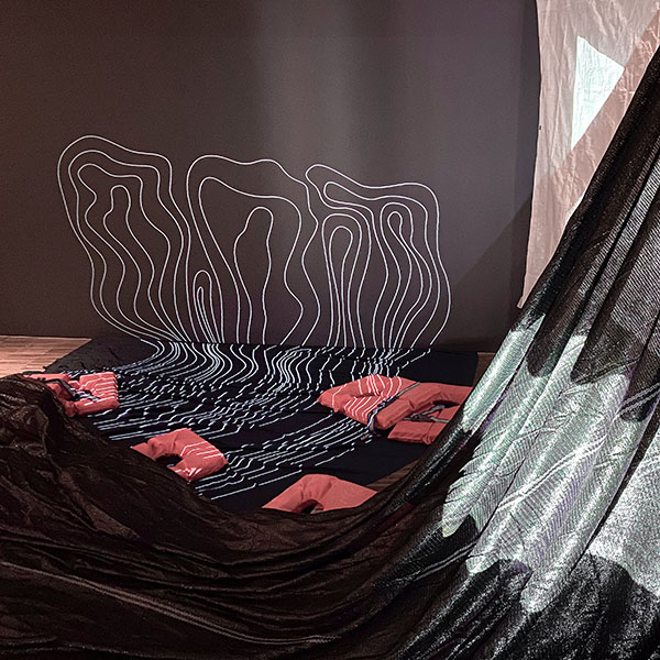 Photograph on an installation, with black plastic sheets, red life jackets and abstract figures projected onto a black screen