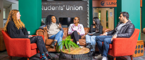 Photograph of five students sitting together in the Students Union, orange armchairs surrounding a circular table.