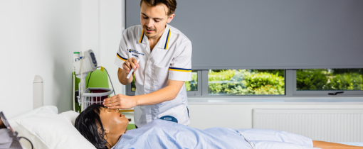 A student in white nursing clothes inspecting a model patient.