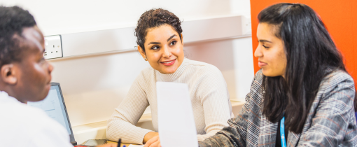 Three people sat together at a table, looking across at each other and conversing.