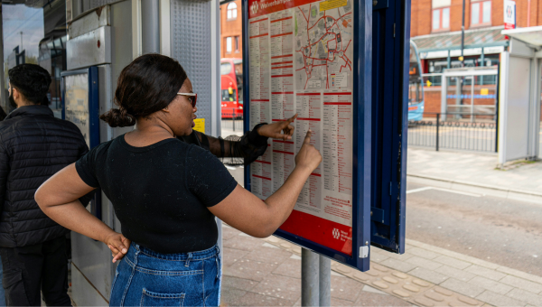 Two students in a bus stop in Wolverhampton, pointing at the provided map to plot their route