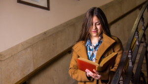A person walking down a staircase reading a large red book.