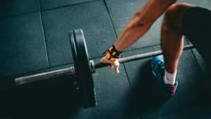 A person at the gym preparing to lift a barbell weight: they are wearing an armband and blue shoes