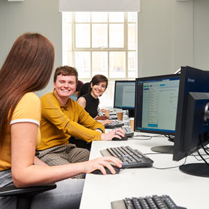 3 students sitting a long table in front of pc's talking