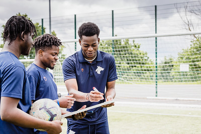 Students practicing coaching in an outdoor area at Walsall Campus, one student showing two others a whiteboard