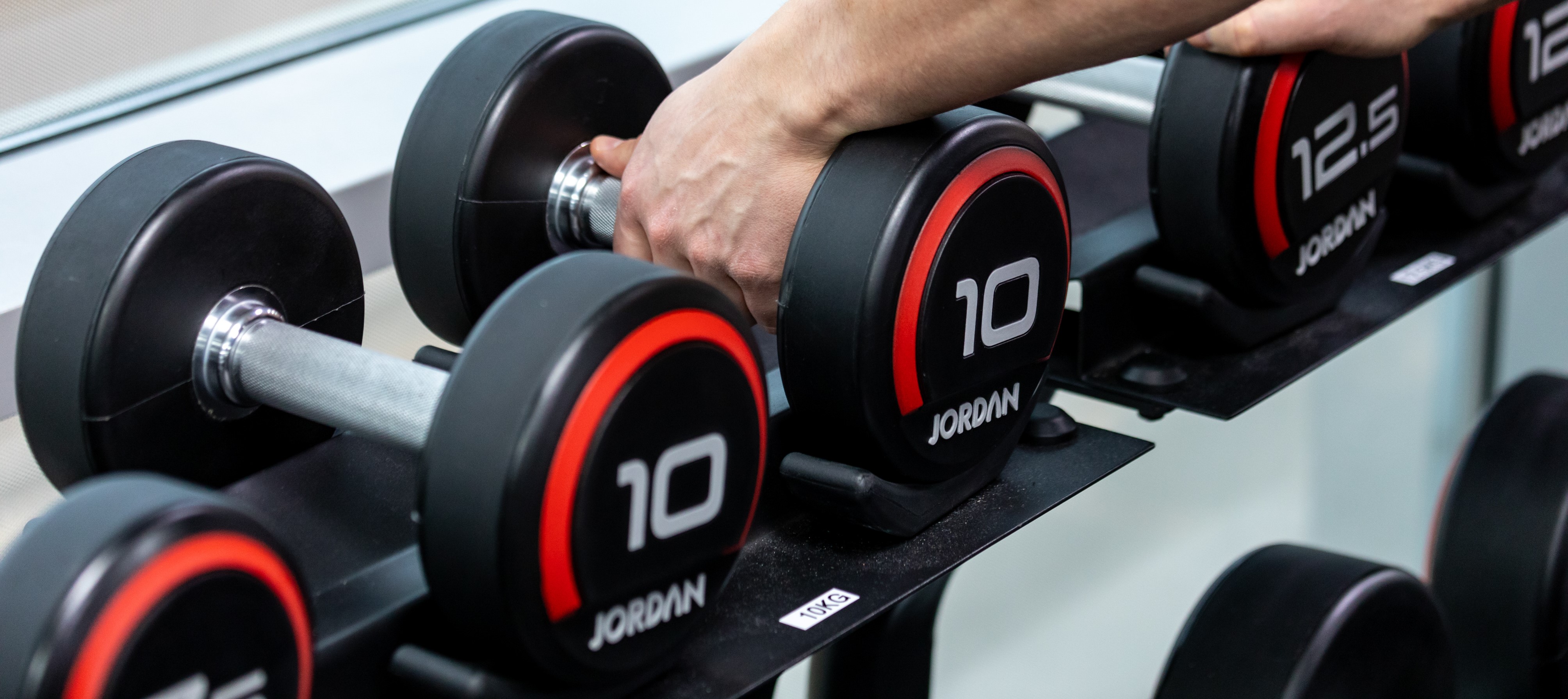Photograph of a dumbbell weight rack, a pair of hands picking up two 10kg weights.