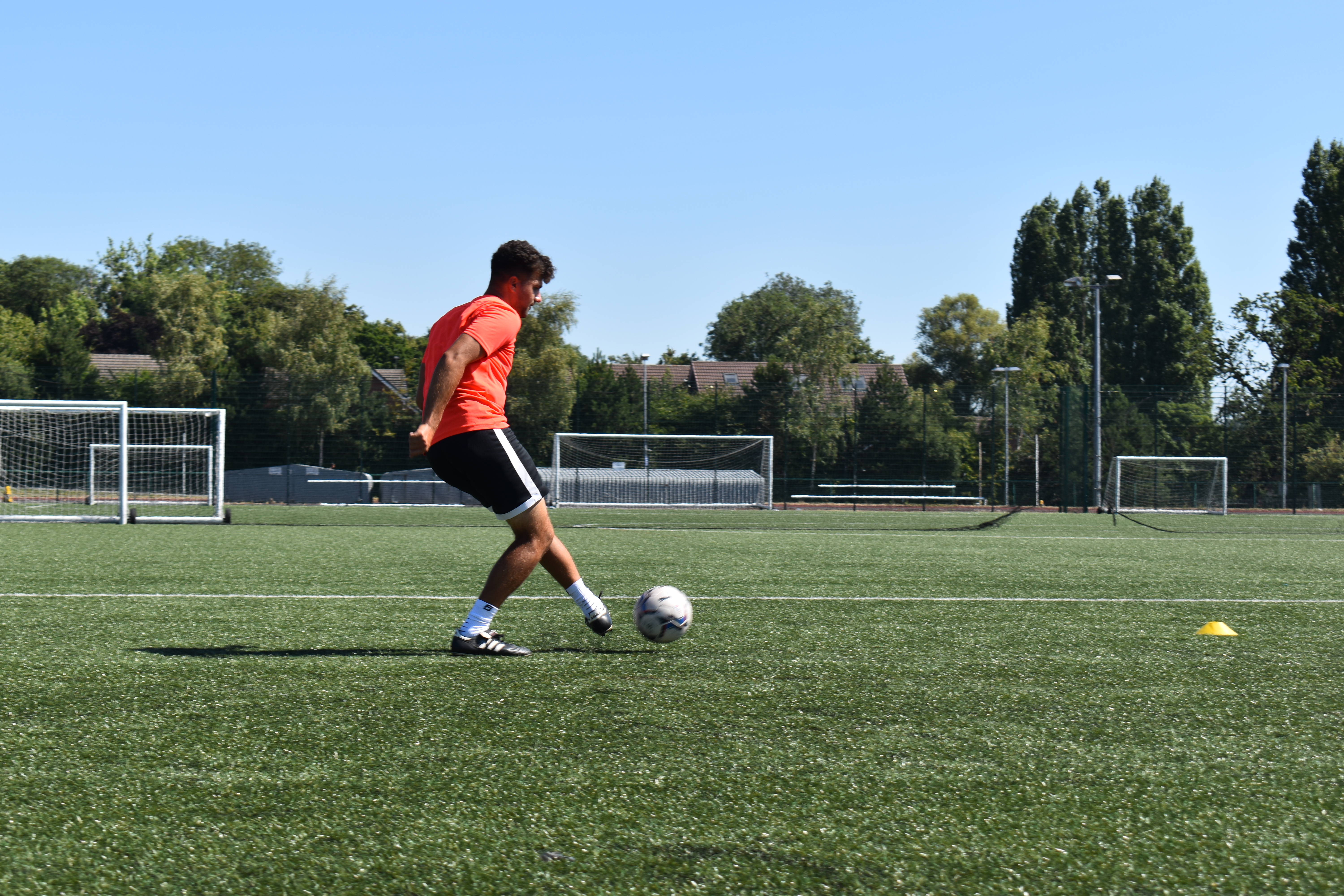 Student at Walsall Campus kicking a football on a field area