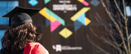 A photograph of a female graduate looking up at the University of Wolverhampton motto
